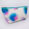 Colorful tie-dye cosmetic bag with pink, blue, green, and purple patterns, featuring a gold zipper, ideal for storing skincare and makeup essentials at The Wraperie.