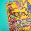 Vibrant silk scarf featuring a tiger, colorful exotic birds, tropical flowers, and intricate patterns on a bright yellow background, showcasing luxury fashion accessories from The Wraperie.