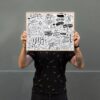 Bright black and white doodle artwork featuring upbeat phrases and icons, held by a person with tattoos, emphasizing creativity and artistic design.