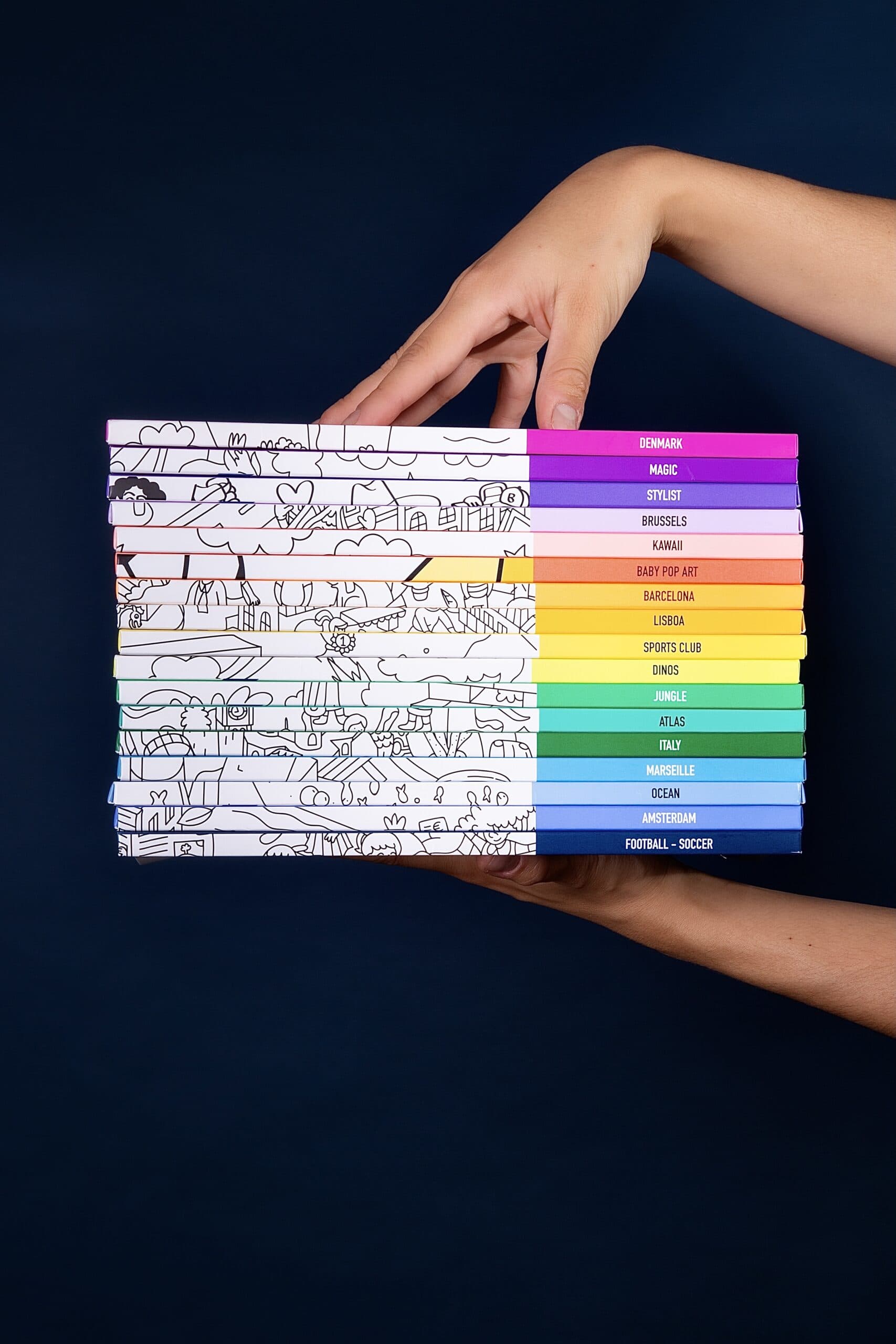 Colorful collection of illustrated books with titles related to travel, culture, and sports held by a hand against dark background.