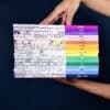 Colorful stack of illustrated notebooks featuring travel and city-themed designs, branded with 