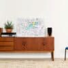 Modern interior decor with a vintage wooden sideboard, a potted succulent, a colorful city map artwork, black and wooden speakers, and a blue accent chair on a beige shag rug.