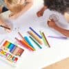 Colorful markers and kids drawing happy faces on paper at The Wraperie, a fun and creative place for children’s activities and art crafting.