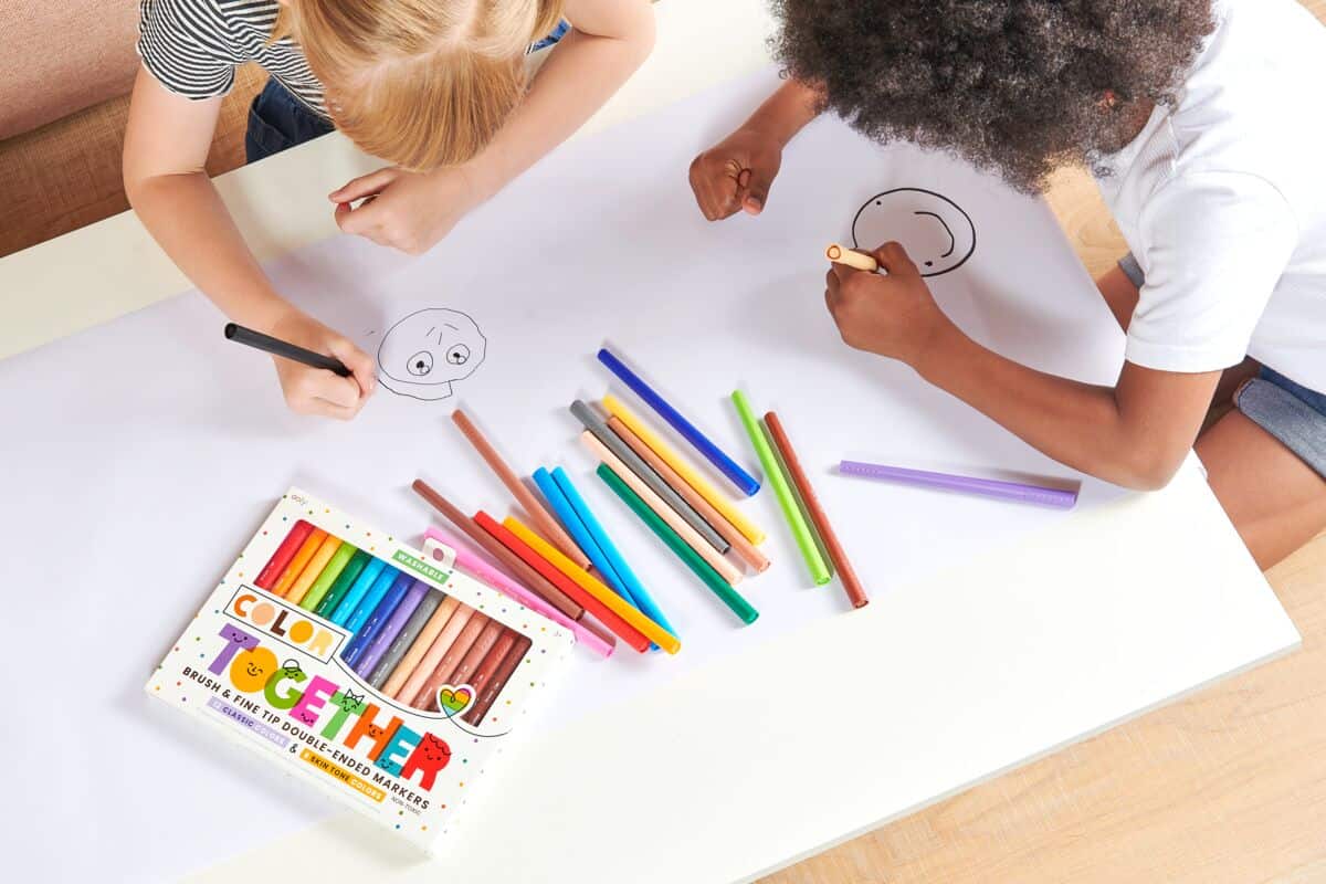 Colorful markers and kids drawing happy faces on paper at The Wraperie, a fun and creative place for children’s activities and art crafting.
