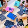 Coloring books with unicorn and dragon designs on black pages, kids drawing with white markers, outdoor art activity, creative kids fun, The Wraperie craft session, inspiring imagination and artistic skills.