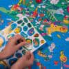 Cute illustrated world map puzzle by The Wraperie featuring vibrant colors and detailed landmarks. Perfect for kids’ educational activities and family fun open-ended play.