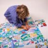 Colorful cityscape puzzle being assembled by a child on a white surface, showcasing detailed illustrations and various landmarks.