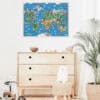 Colorful illustrated world map poster hanging in a modern nursery with light wooden furnishings and decorative elements.