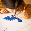 Colorful children's artwork featuring a blue dinosaur with red accents, created with paints and a fine brush, showcasing young artistic talent and creativity.
