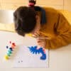 Colorful kid painting a dragon craft, sitting at a white table with paint pots, creative art activity, kids' craft, arts and crafts for children, learning and fun at The Wraperie.