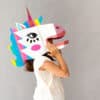 Colorful unicorn-themed cardboard costume for kids with artistic face designs and vibrant decorations. Perfect for children's parties and creative dress-up fun.