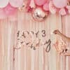 Bright pink and rose gold birthday decorations with balloon garland, "Happy 3rd Birthday" banner, and tissue paper flowers creating a festive atmosphere for a child's celebration.
