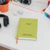 Bright lime green positive student planner with cute black eyelash illustration, placed on a white desk with stationery and accessories for organization and motivational planning.