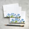 Vibrant blue floral-themed stationery set with matching cards and envelopes, perfect for personalized notes or special occasions, on a marble surface with a black pencil.