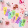 Colorful confetti cake toppers with numbers on pastel paper cards, surrounded by sprinkles, balloons, and party decor for birthday celebration, from The Wraperie.