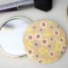 Mini floral fabric mirror with makeup brushes and jewelry on a white surface.