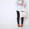 Handbag with bird illustration and inspirational quote, carried by a woman in casual fashion standing against a white wall.
