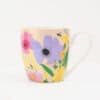 Vibrant floral patterned ceramic mug with colorful flowers, green leaves, and a bee, perfect for coffee or tea lovers, showcasing The Wraperie’s artistic and eco-friendly drinkware collection.