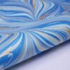 Vibrant blue, white, and gold marbled wrap paper with swirling patterns, perfect for gift wrapping and packaging at The Wraperie.