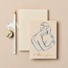 Soft beige background with a romantic greeting card featuring a minimalist blue line art of a couple embracing, and "I love you" written in gold; accented by a white pencil, flower, and tape.