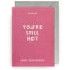 Bright pink anniversary greeting card with "You're Still Hot" message and white text, presented with an elegant gray envelope for celebrating love and special occasions.