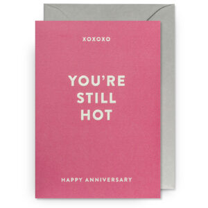 Bright pink anniversary greeting card with "You're Still Hot" message and white text, presented with an elegant gray envelope for celebrating love and special occasions.