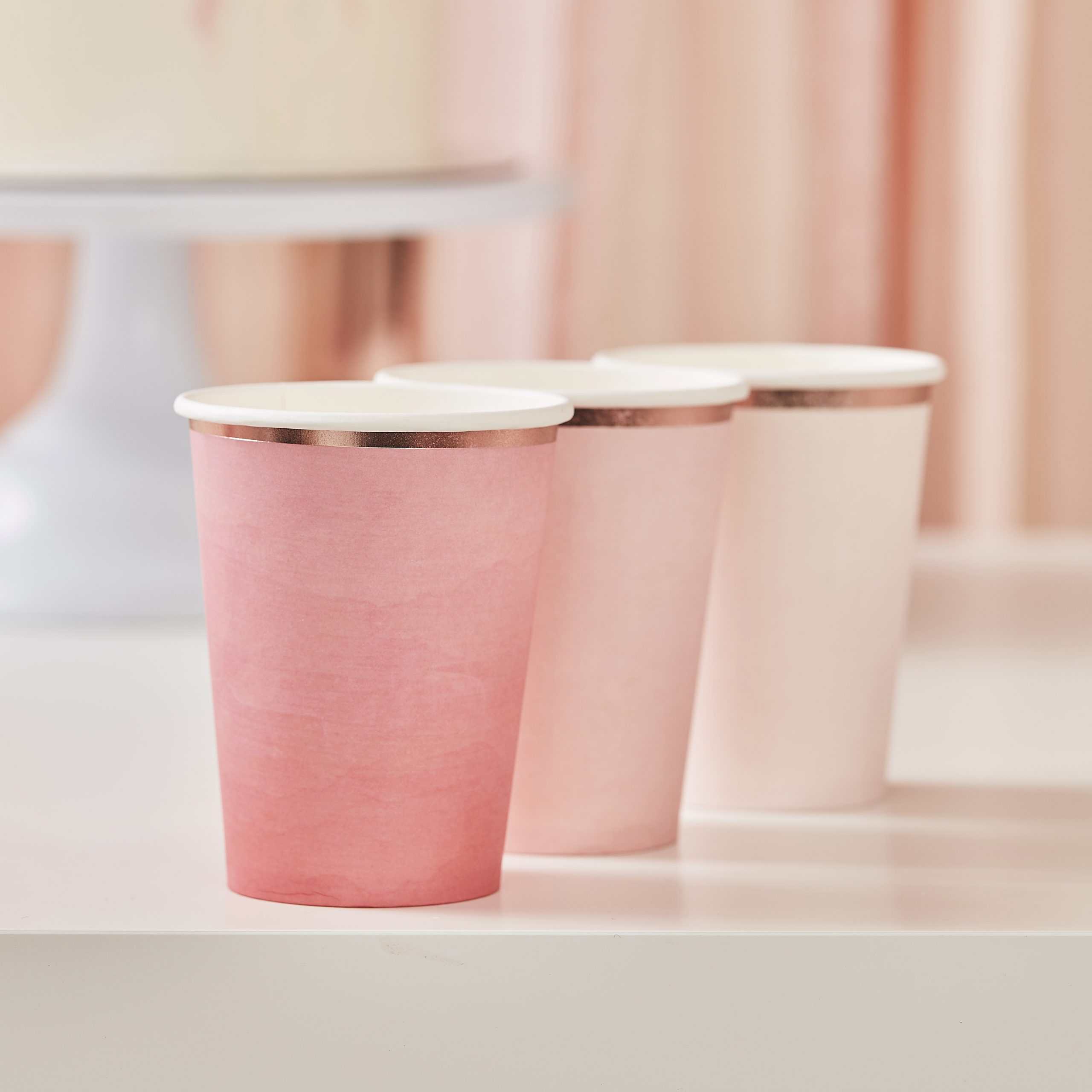 Pink paper coffee cups with white lids on a white surface at The Wraperie.