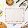 Colorful weekly planner with floral design on a white desk, decorated with stationery and a glass of water, promoting organization and productivity.