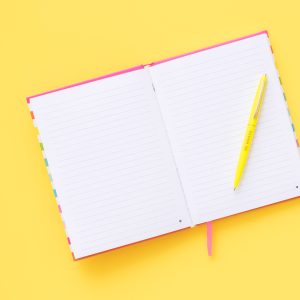 Bright open notebook with lined pages and a yellow pen on a vibrant yellow background, ideal for journaling, planning, or note-taking.