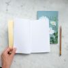 Open dotted notebook with yellow grid notebook behind on marble surface, floral art card and gold pen.