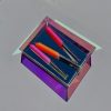 Bright pink, orange, and pink highlighters inside a reflective, geometric acrylic container on a minimalist gray surface.