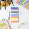 Colorful rainbow-themed to-do list notepad with pens, paper clips, and stationery on white desk for organization and planning.