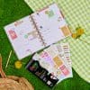 Bright, colorful planner open on green grass with doodle stickers and decorative elements, showcasing creative organization tools and planner accessories from The Wraperie.
