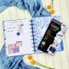 Bright blue and white floral planner open to February 2023 with colorful stickers, surrounded by yellow flowers and a blue scarf, showcasing stylish organization tools for planning and scheduling.
