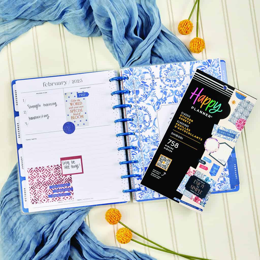 Bright blue and white floral planner open to February 2023 with colorful stickers, surrounded by yellow flowers and a blue scarf, showcasing stylish organization tools for planning and scheduling.