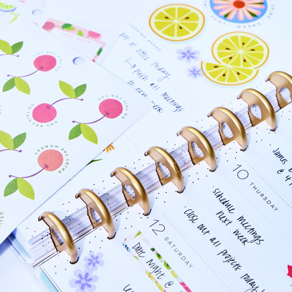 Chocolate gold rings on a day planner along with colorful stickers and notes, showcasing planning, organization, and motivational journaling tools at The Wraperie.