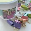 Colorful pastel binder clips in various shades including purple, pink, blue, green, and peach, scattered around a clear plastic container, perfect for office or craft organization.