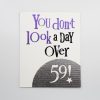 Colorful motivational quote print from The Wraperie, featuring a playful design with the phrase "You don't look a day over 59" on a white background, perfect for inspiring daily positivity.