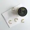 Delicate gold crescent moon paper clips from The Wraperie on white paper with black candle tin, showcasing premium stationery and desk accessories with elegant celestial design.