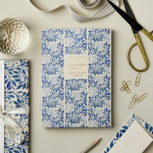 Vibrant blue floral weekly planner by Wanderlust Paper Co. surrounded by gift wrapping supplies and office tools on a clean, neutral background. Perfect for organization and stationery enthusiasts.