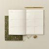 Blank weekly planner with floral-patterned notebook, gold pen, paper clips, and a staple on a neutral background for organization and productivity.