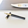 Stylish black and gold fountain pen on a white desk, modern office setting, with a decorative plate and gold pushpins in the background, perfect for luxury writing accessories.