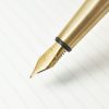 Luxurious gold fountain pen nib on lined paper, illustrating premium writing instruments from The Wraperie. Ideal for showcasing elegant stationery and personalized pen accessories.