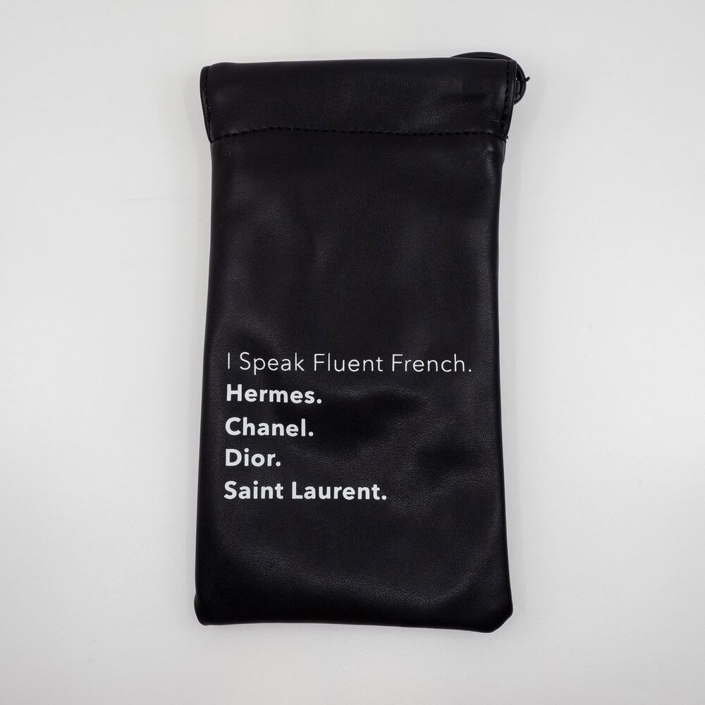 Luxury designer clutch with white text featuring high-end brands Hermes, Chanel, Dior, Saint Laurent on black faux leather accessory for fashion enthusiasts.