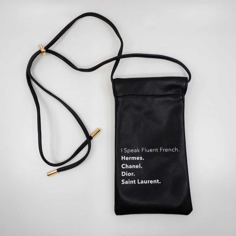 Elegant black leather crossbody bag with removable strap, featuring iconic luxury brand names on the front. Perfect accessory for fashion-forward outfits.