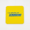 Bright yellow coaster with bold blue text reading “I am definitely not demanding” showcasing humorous and playful message. Perfect for fun gatherings or as a quirky gift.