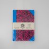 Bright blue and pink patterned notebook with a white band, handmade and artisanal, since 1918, on a white surface - ideal for creative writing, note-taking, or journaling.