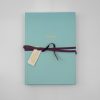 Aqua-colored notebook with "Compose" written in gold, tied with a dark purple ribbon and a small tag, ideal for creative writing or note-taking.