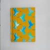 Bright yellow notebook cover featuring vibrant blue hummingbird illustrations, perfect for journaling, note-taking, or customizing with your own designs. An eye-catching accessory for stationery lovers.