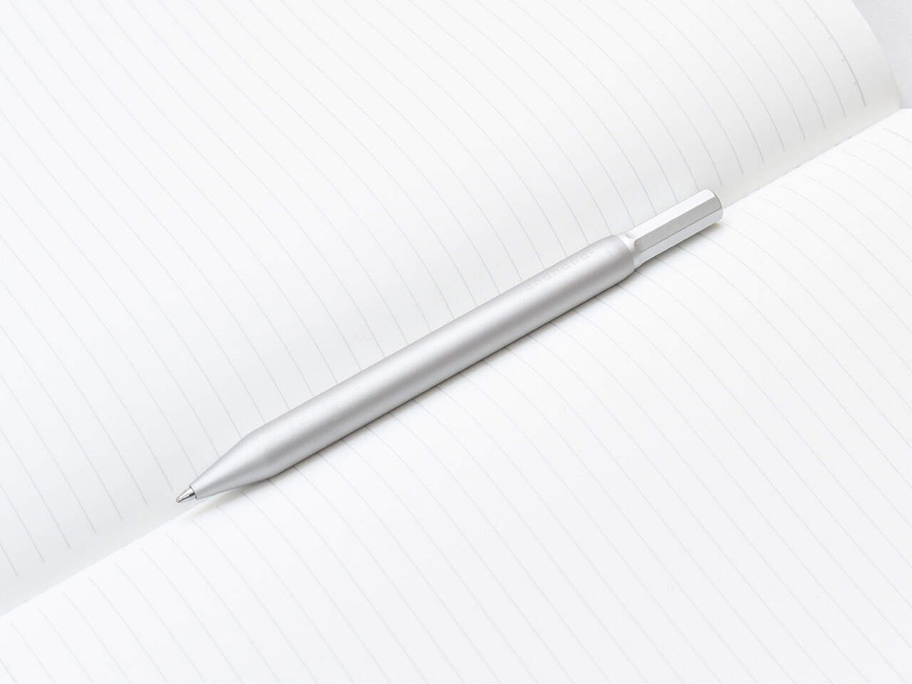A sleek silver pen resting on an open, lined notebook page for writing or note-taking.